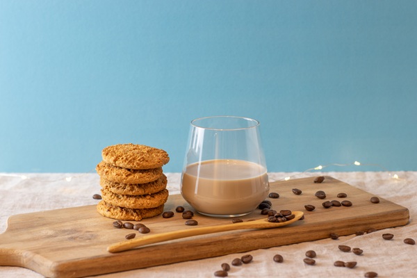 Stack of cookies and glass of coffee on cutting board with coffee beans against a blue background