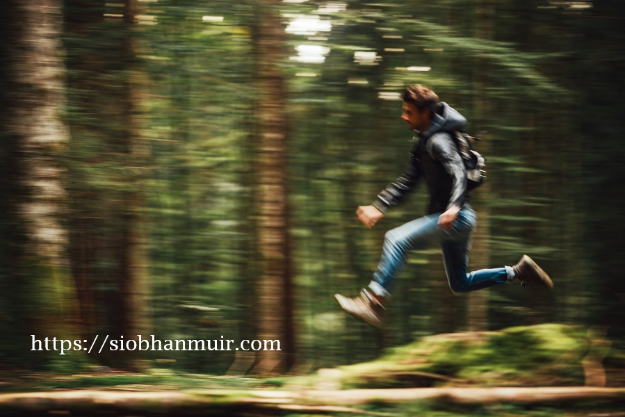 Man running through a forest with jeans and a backpack