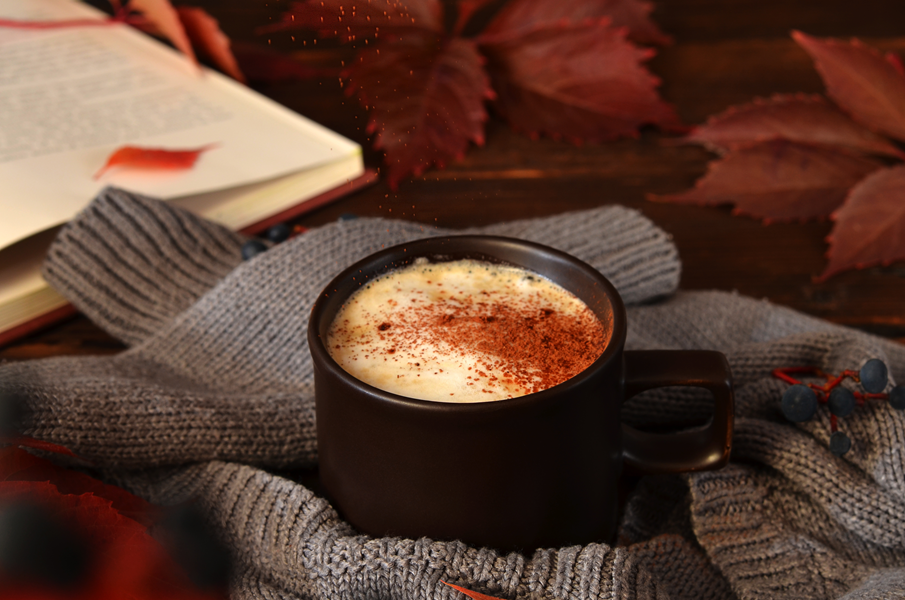 Cup of chai on a gray sweater with a book and leaves in the background